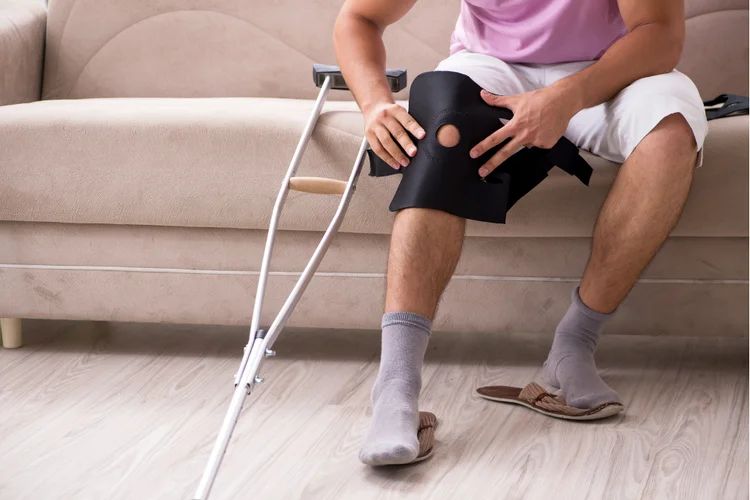 Man sitting with knee brace and crutches after ACL tear.