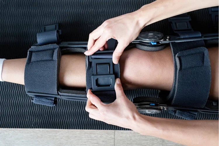 Hands adjusting knee brace during ACL rehab.