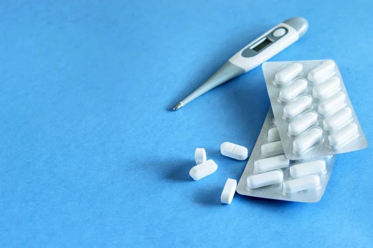 White tablets and thermometer representing anti-inflammatory medication for orthopaedic pain relief.