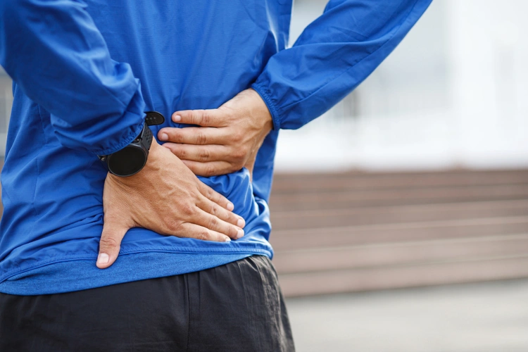 Asian man holding lower back in discomfort showing symptoms of lower back pain and muscle strain.