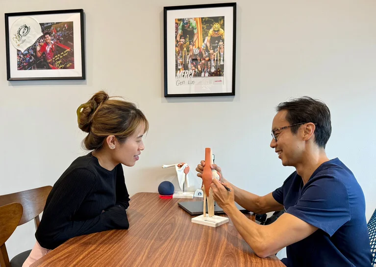Dr Foo Gen Lin using knee joint model to explain cartilage damage to female patient.