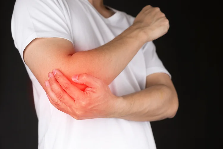 Man in white shirt holding red elbow, showing possible tendon or nerve-related pain.