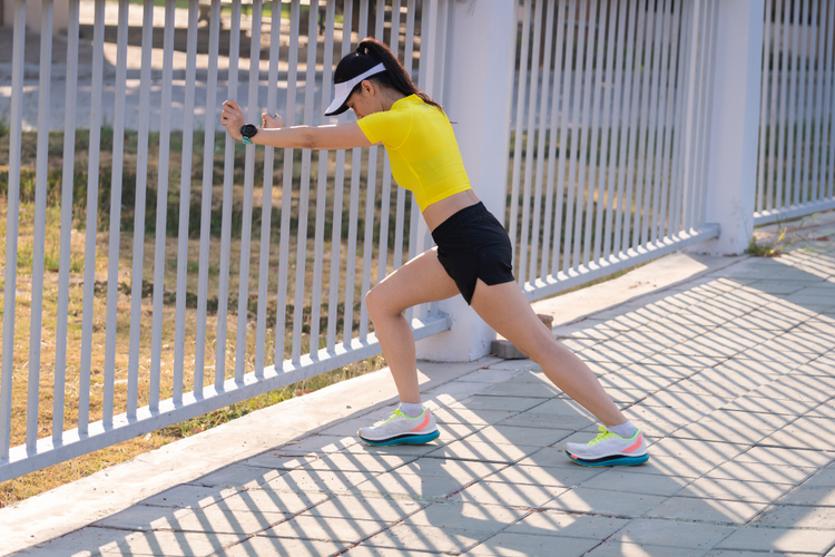Female runner stretching calves before training to prevent post-marathon knee pain in future races.