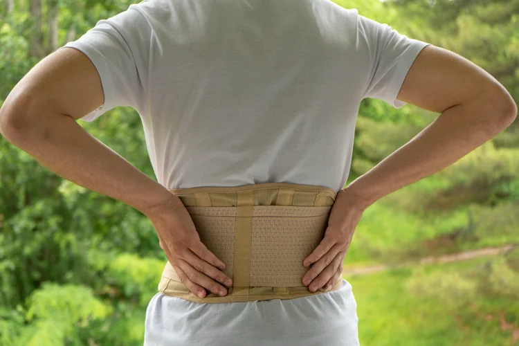 Man using lumbar support brace outdoors for spine recovery.