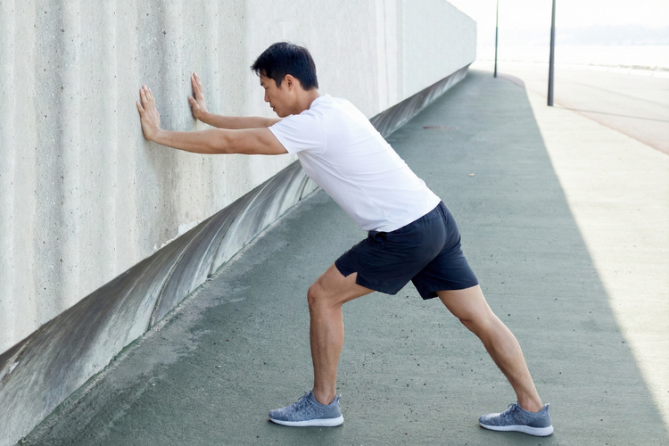 Man doing a calf stretch as part of stretching exercises for knee pain to ease muscle tightness.