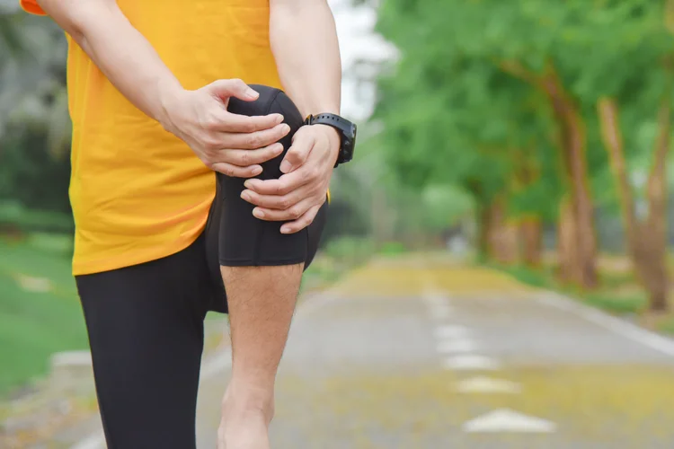 Man holding knee outdoors emphasising importance of stretching before exercise to prevent knee pain.