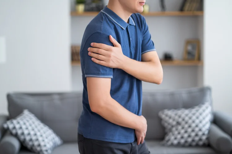 Man experiencing limited shoulder movement due to collarbone pain from injury.