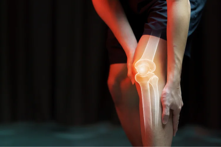 Person holding their knee with a visible highlighted joint illustration, symbolising knee pain and injury, with possible causes like arthritis or ligament damage.