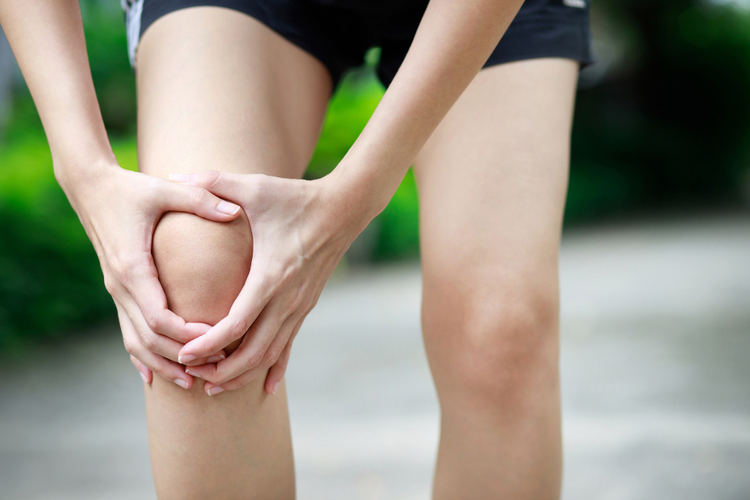 Person holding painful knee outdoors, considering exercises for knee pain to improve movement.