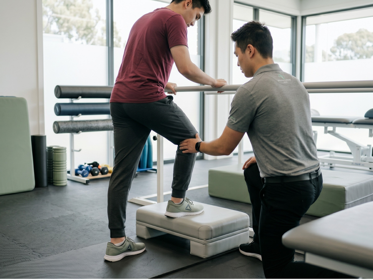 Physiotherapist guiding a patient through a step-up exercise in a clinic.