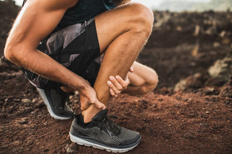 Runner clutching ankle after Achilles tendon rupture on trail.