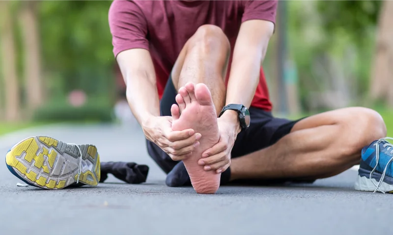 Male runner holding heel and arch due to plantar fasciitis pain on outdoor track.