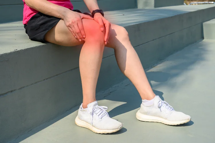 Female runner holding outer knee in pain from IT band syndrome, an overuse injury.