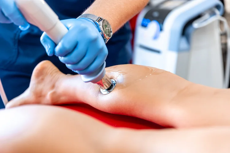 Shockwave therapy performed on heel using handheld device with conductive gel in orthopaedic clinic.