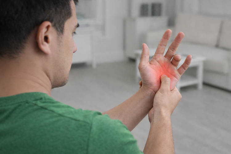 Man pressing painful palm highlighted in red showing trigger finger symptoms.