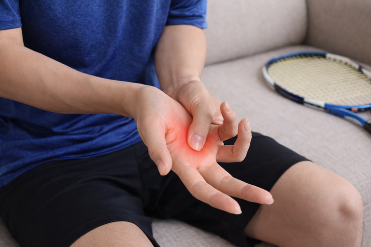 Athlete holding painful palm highlight in red due to trigger finger condition.