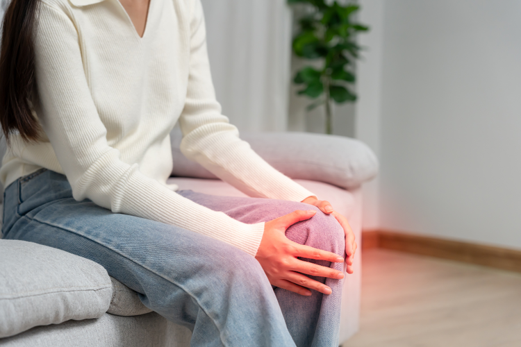 Woman holding painful knee sitting on sofa, experiencing post-marathon knee discomfort at home.