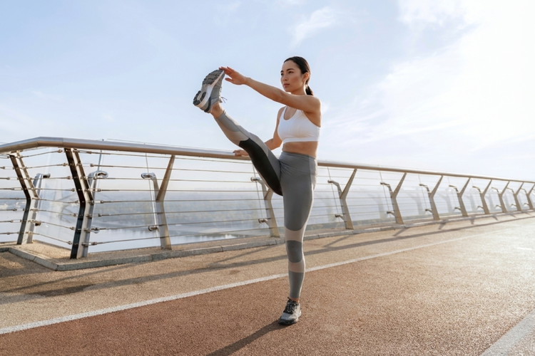 Woman performing leg swings to warm hip flexors and hamstrings as part of dynamic pre-run stretches.