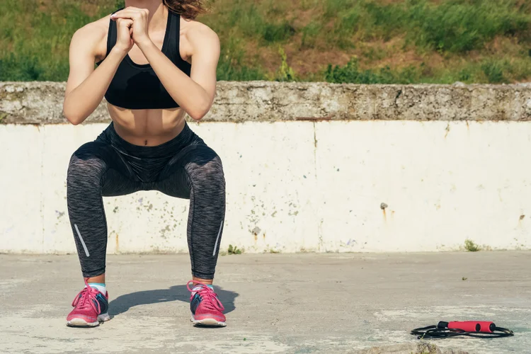 Woman performing squat exercise outdoors to strengthen leg muscles and help prevent runner’s knee.