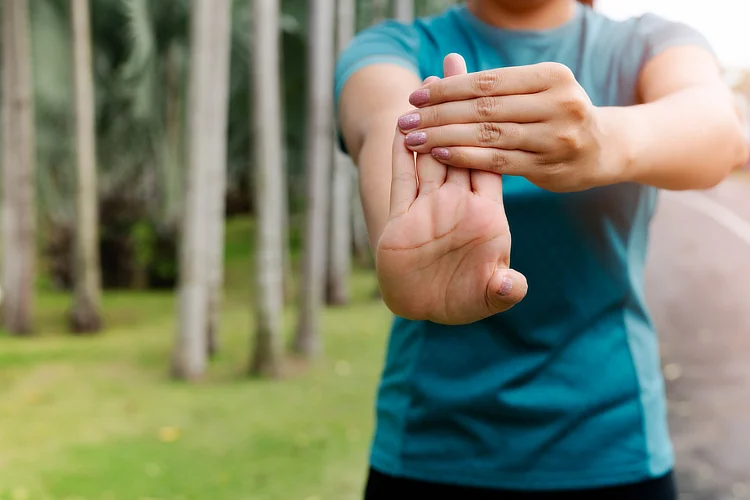 Woman stretching wrist outdoors to prevent elbow pain from repetitive strain.